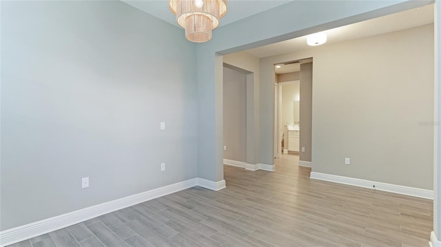 empty room featuring a notable chandelier and light wood-type flooring