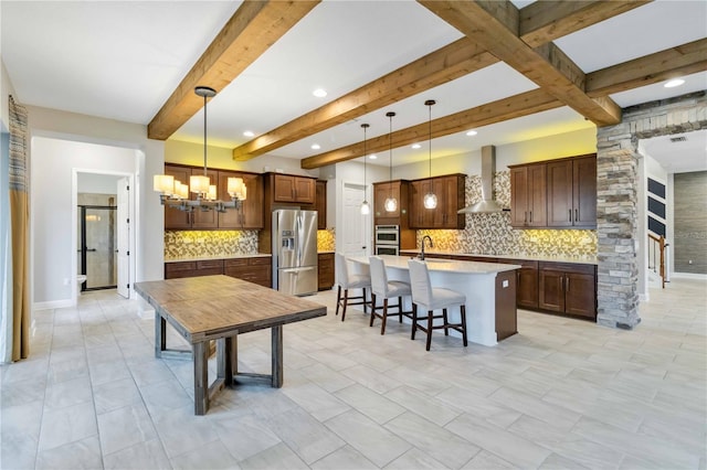 kitchen with appliances with stainless steel finishes, decorative light fixtures, tasteful backsplash, and wall chimney range hood