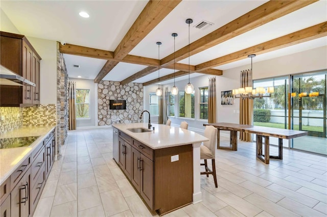 kitchen featuring black electric cooktop, a kitchen island with sink, sink, dishwasher, and hanging light fixtures