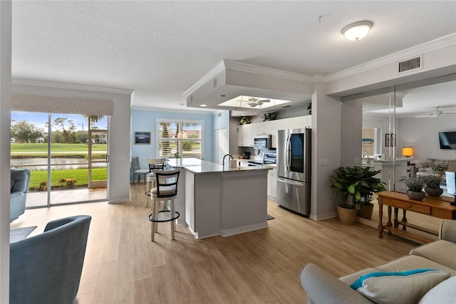 kitchen featuring white cabinets, appliances with stainless steel finishes, light hardwood / wood-style flooring, and ornamental molding