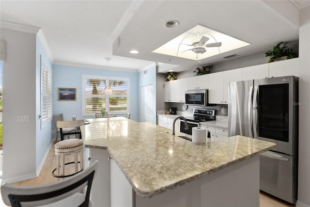 kitchen featuring a kitchen island with sink, crown molding, appliances with stainless steel finishes, light stone counters, and white cabinetry