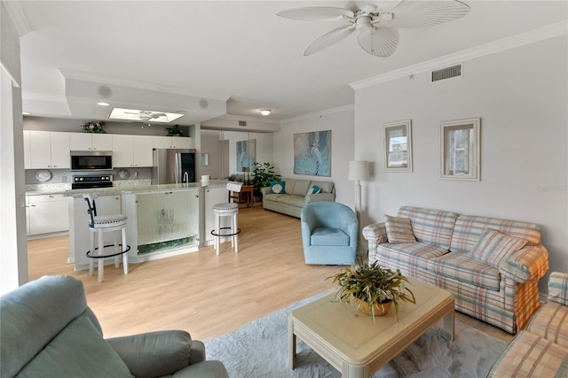 living room with a skylight, ceiling fan, light hardwood / wood-style floors, and ornamental molding