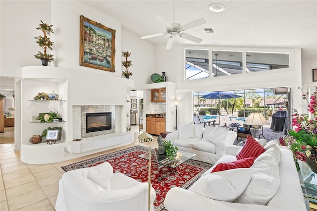 tiled living room with a textured ceiling, a towering ceiling, ceiling fan, and a premium fireplace