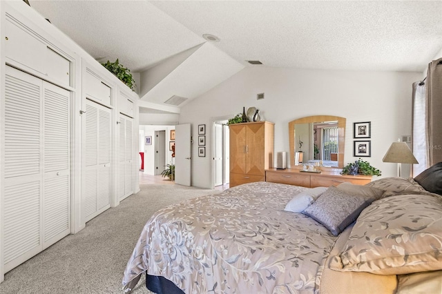 bedroom with a textured ceiling, lofted ceiling, light colored carpet, and multiple closets