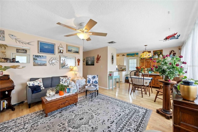 living room featuring ceiling fan, light wood-type flooring, and a textured ceiling