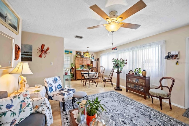 living room featuring a textured ceiling, light hardwood / wood-style floors, plenty of natural light, and ceiling fan