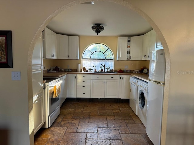 kitchen with washer / dryer, white appliances, white cabinetry, and sink