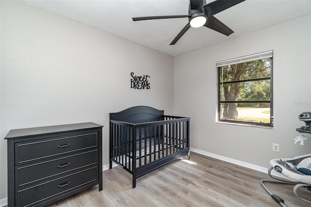 bedroom featuring ceiling fan, light hardwood / wood-style floors, and a nursery area