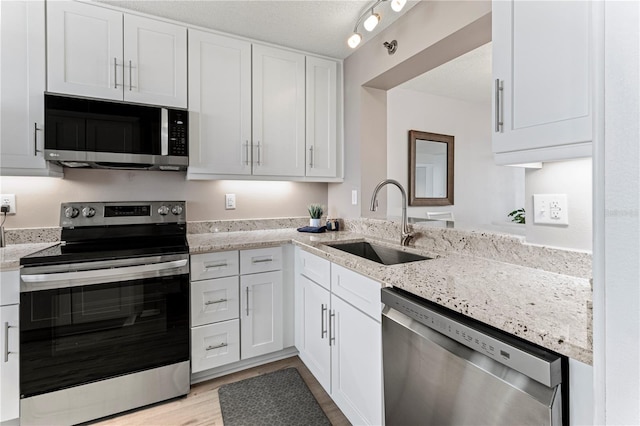 kitchen featuring sink, light stone countertops, a textured ceiling, appliances with stainless steel finishes, and white cabinetry