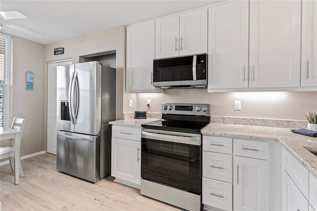 kitchen with white cabinets, light hardwood / wood-style flooring, light stone countertops, a textured ceiling, and stainless steel appliances