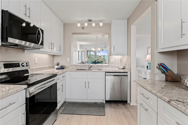 kitchen featuring white cabinetry, stainless steel appliances, an inviting chandelier, a textured ceiling, and light wood-type flooring