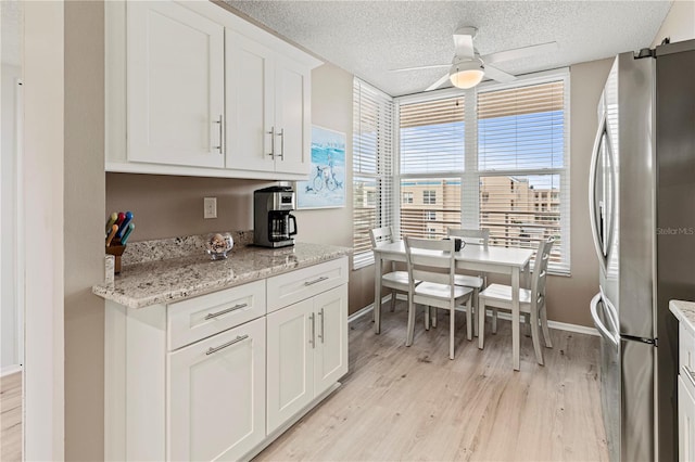 kitchen with light wood-type flooring, a textured ceiling, ceiling fan, white cabinets, and stainless steel refrigerator