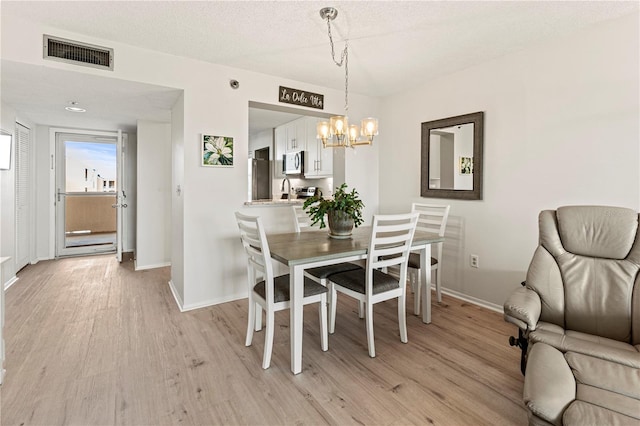 dining area with light hardwood / wood-style flooring, a textured ceiling, and an inviting chandelier