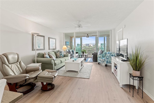 living room featuring ceiling fan, expansive windows, light hardwood / wood-style floors, and a textured ceiling