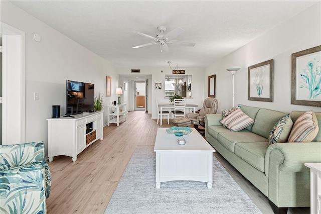 living room with light hardwood / wood-style flooring, ceiling fan with notable chandelier, and a textured ceiling