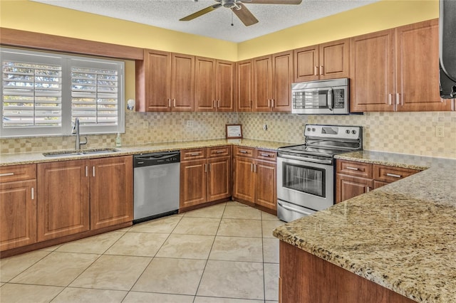 kitchen with sink, light stone counters, backsplash, a textured ceiling, and appliances with stainless steel finishes