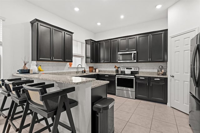 kitchen with sink, a breakfast bar area, light stone counters, appliances with stainless steel finishes, and kitchen peninsula