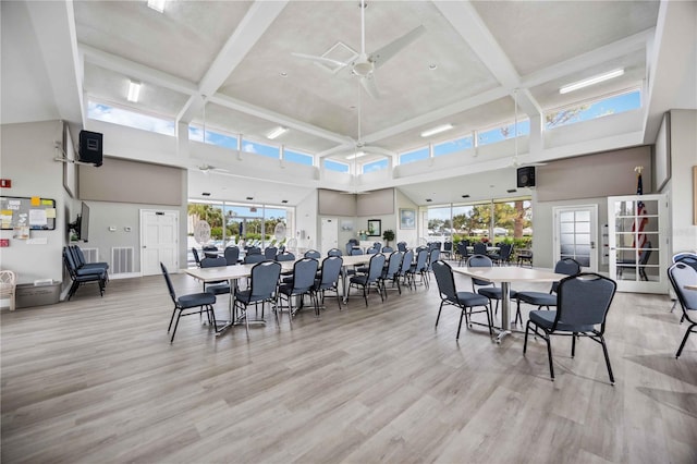 dining space with ceiling fan, beam ceiling, a high ceiling, and light hardwood / wood-style flooring