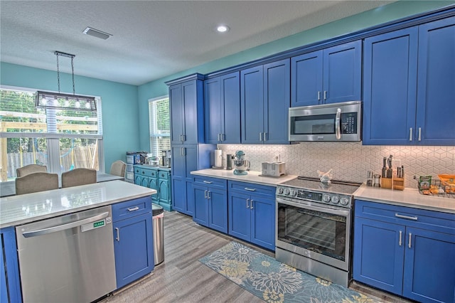 kitchen with blue cabinets, backsplash, pendant lighting, light hardwood / wood-style floors, and appliances with stainless steel finishes