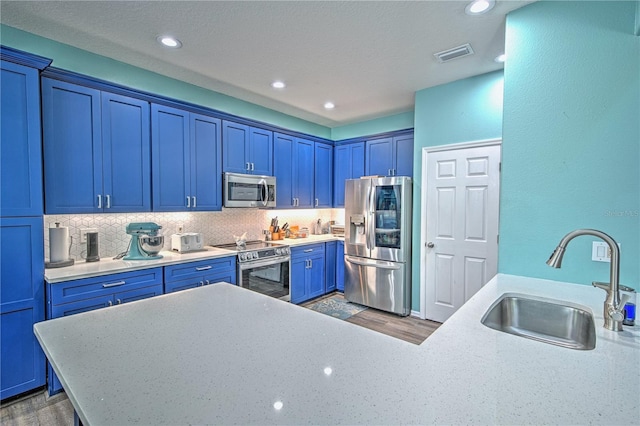 kitchen with appliances with stainless steel finishes, backsplash, dark wood-type flooring, sink, and blue cabinetry