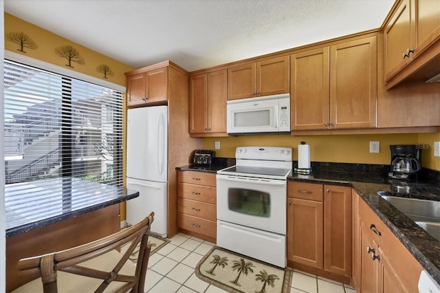 kitchen featuring a textured ceiling, light tile patterned floors, dark stone counters, and white appliances