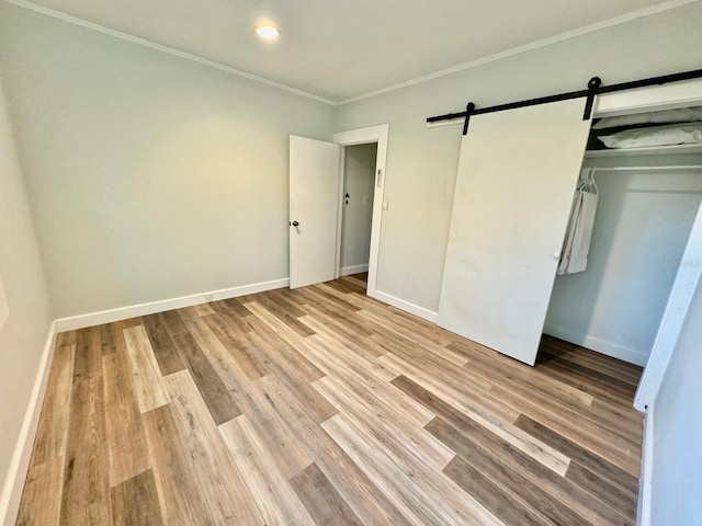 unfurnished bedroom with a barn door, light wood-type flooring, crown molding, and a closet