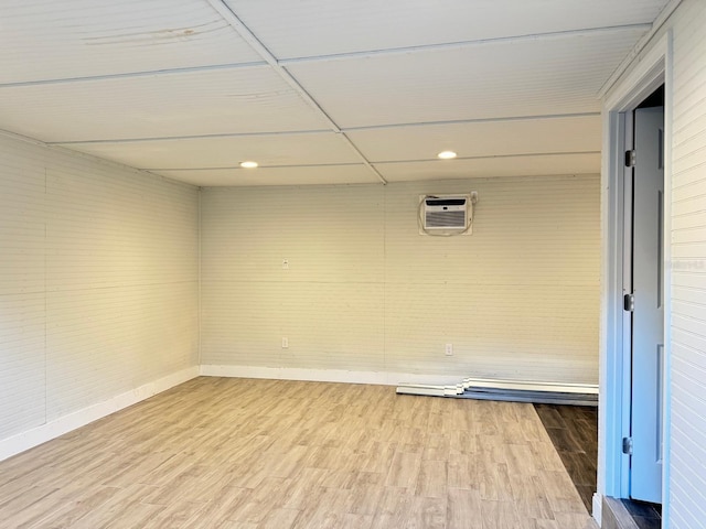 basement featuring an AC wall unit, a paneled ceiling, and wood-type flooring