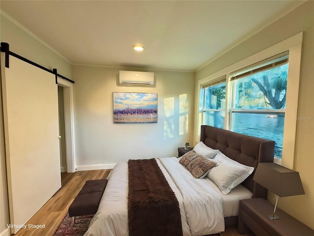 bedroom featuring a wall unit AC, a barn door, hardwood / wood-style floors, and ornamental molding