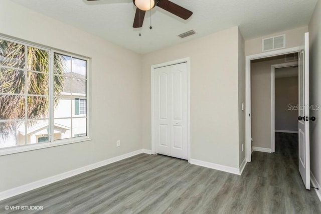 unfurnished bedroom featuring a textured ceiling, a closet, ceiling fan, and dark wood-type flooring