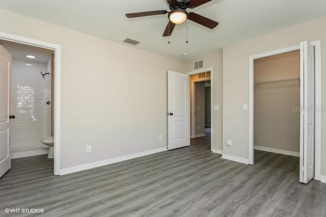 unfurnished bedroom featuring connected bathroom, ceiling fan, dark wood-type flooring, a walk in closet, and a closet