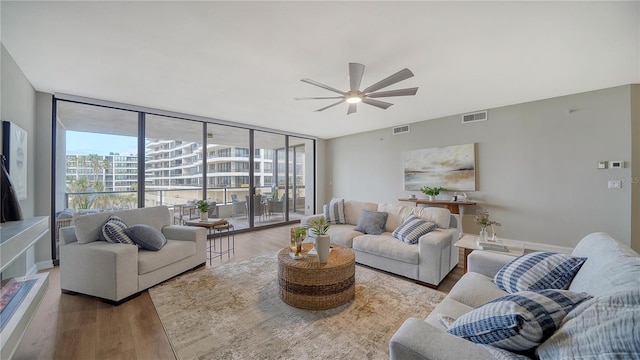 living room with wood-type flooring, expansive windows, and ceiling fan