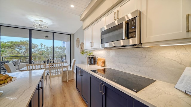 kitchen featuring blue cabinets, black electric cooktop, light hardwood / wood-style floors, light stone counters, and white cabinetry