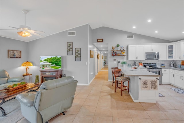 kitchen featuring appliances with stainless steel finishes, light stone countertops, white cabinets, a kitchen bar, and decorative backsplash