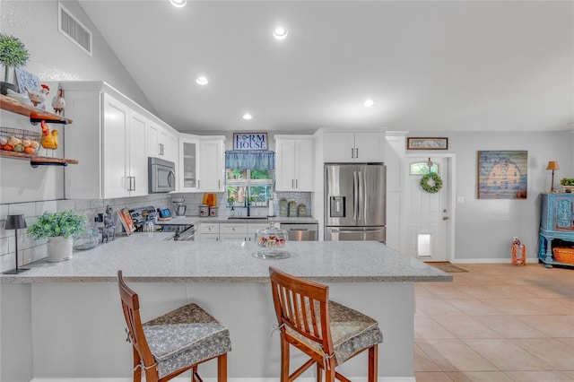 kitchen featuring white cabinets, a kitchen breakfast bar, kitchen peninsula, stainless steel appliances, and light stone countertops