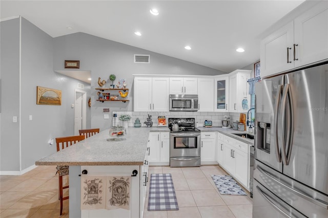 kitchen featuring appliances with stainless steel finishes, lofted ceiling, white cabinets, a kitchen breakfast bar, and kitchen peninsula