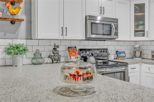 kitchen with tasteful backsplash, light stone counters, stainless steel appliances, and white cabinets