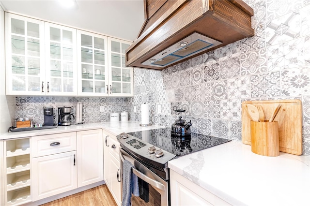 kitchen featuring stainless steel range with electric cooktop, backsplash, white cabinets, custom range hood, and light wood-type flooring