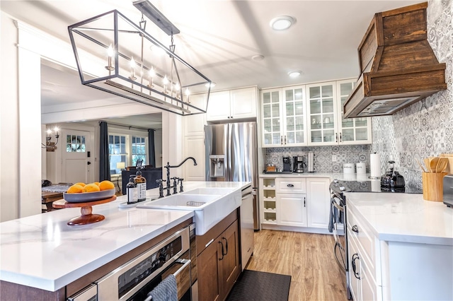 kitchen with backsplash, light hardwood / wood-style floors, a kitchen island with sink, white cabinets, and custom exhaust hood