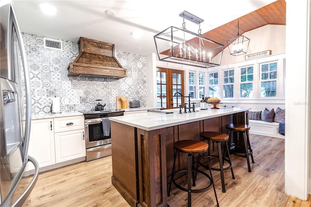 kitchen with premium range hood, stainless steel appliances, pendant lighting, an inviting chandelier, and white cabinets