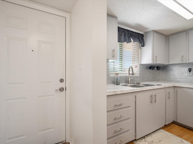 kitchen with tasteful backsplash, sink, a textured ceiling, and light hardwood / wood-style flooring