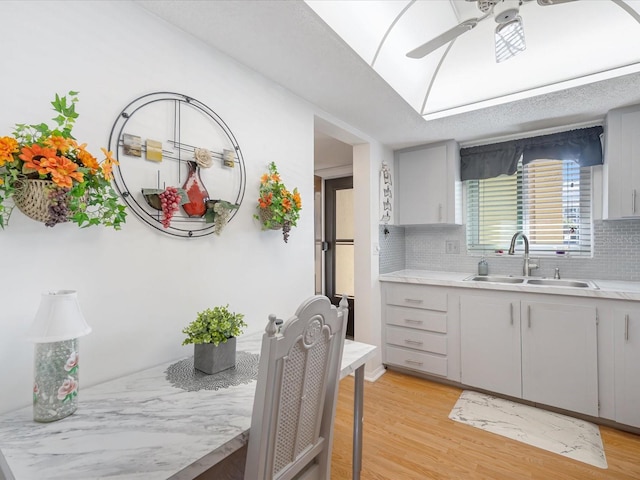 kitchen featuring a breakfast bar, sink, light hardwood / wood-style flooring, decorative backsplash, and ceiling fan