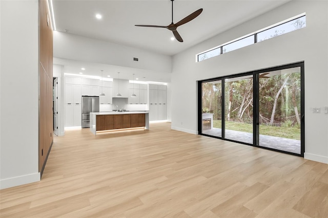 unfurnished living room with ceiling fan, light wood-type flooring, and a high ceiling