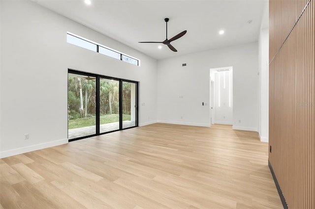 empty room featuring ceiling fan, light wood-type flooring, and a high ceiling