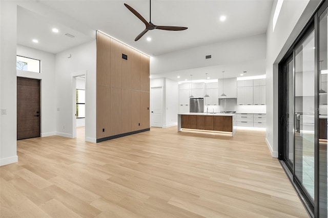 unfurnished living room featuring ceiling fan, sink, a high ceiling, and light hardwood / wood-style flooring