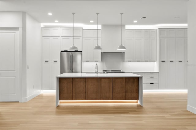 kitchen featuring stainless steel fridge, a center island with sink, pendant lighting, and light hardwood / wood-style floors