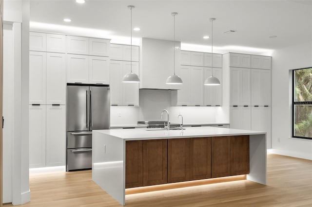 kitchen with stainless steel fridge, light wood-type flooring, and a kitchen island with sink