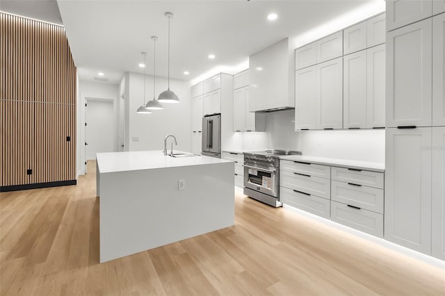 kitchen featuring sink, hanging light fixtures, an island with sink, appliances with stainless steel finishes, and light wood-type flooring