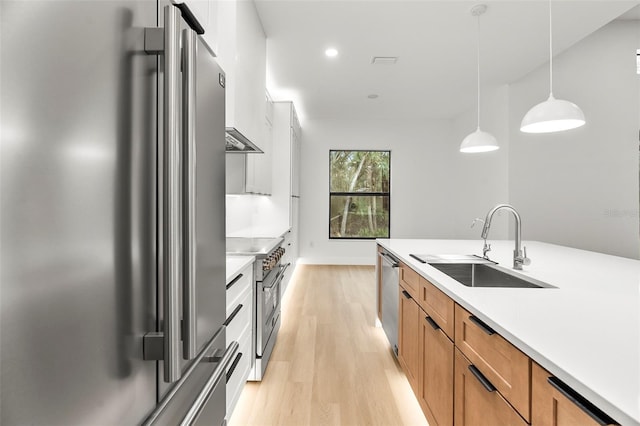 kitchen with sink, stainless steel appliances, decorative light fixtures, and light wood-type flooring