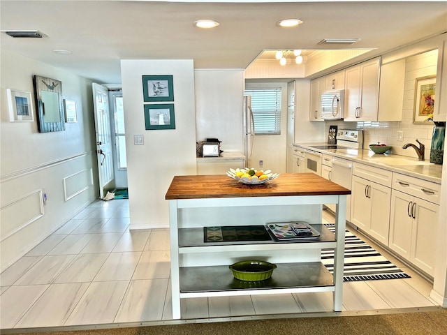 kitchen with butcher block counters, white cabinetry, sink, range with electric cooktop, and decorative backsplash