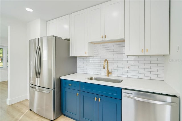 kitchen featuring backsplash, stainless steel appliances, blue cabinets, sink, and white cabinets